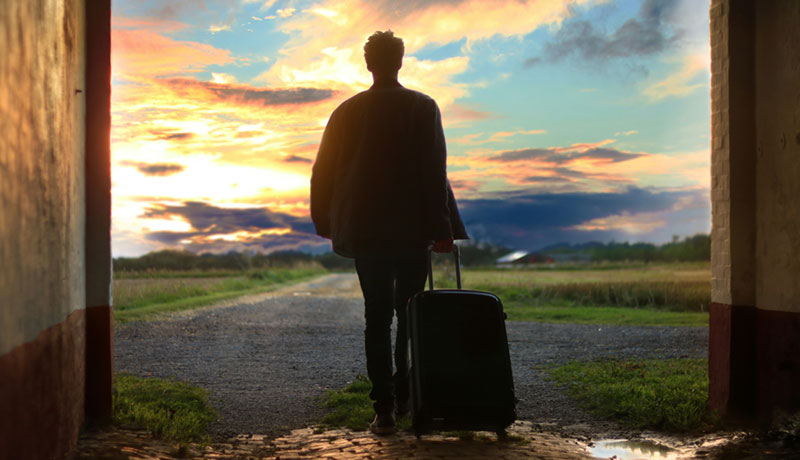 Travel insurance: a person walks out into a wide-open landscape with a suitcase.